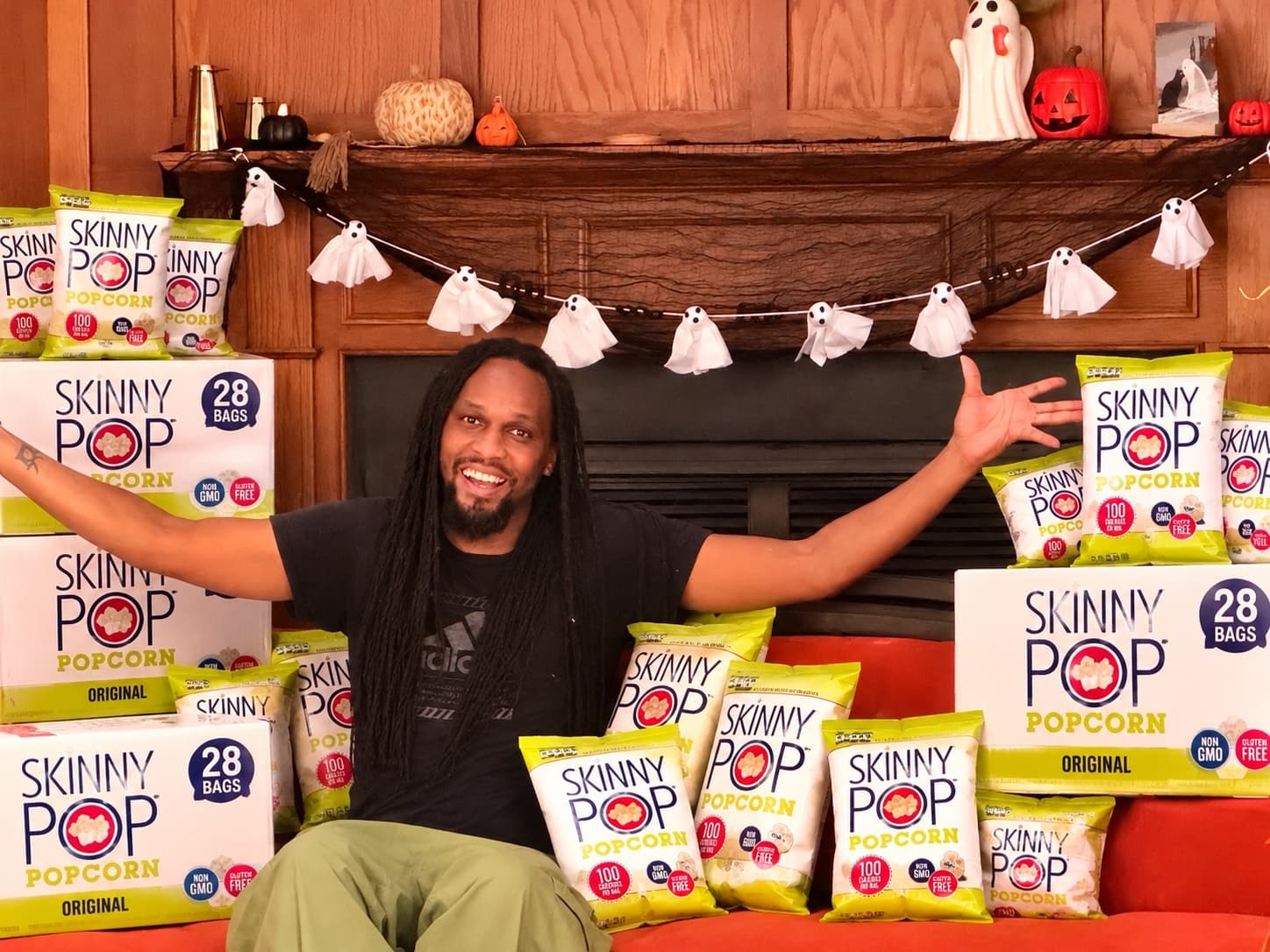 Miami Slim with arms spread wide, surrounded by a fortress of SkinnyPop boxes and bags